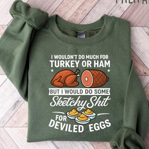 May include: Military green sweatshirt with the text "I wouldn't do much for turkey or ham but I would do some sketchy shit for deviled eggs." The graphic includes images of a turkey, ham, and deviled eggs.