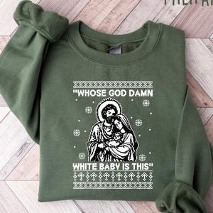 May include: Military green sweatshirt with a white graphic of a religious scene and the text "WHOSE GOD DAMN WHITE BABY IS THIS". The sweatshirt has long sleeves and a crew neck.