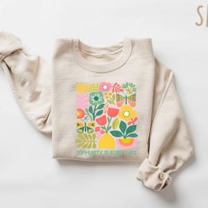 May include: A beige sweatshirt with a colorful floral design and the text "Community is Resistance" printed on the front.