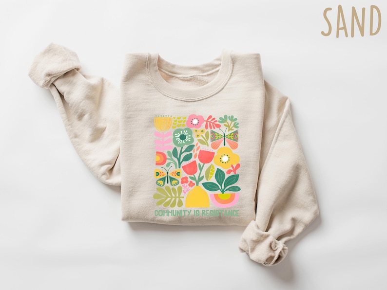 May include: A beige sweatshirt with a colorful floral design and the text "Community is Resistance" printed on the front.
