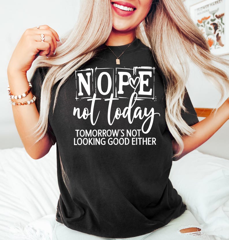 May include: Black t-shirt with the words "NOPE not today" in white, along with the phrase "TOMORROW'S NOT LOOKING GOOD EITHER." The shirt has a crew neck and short sleeves. The shirt is worn by a person.
