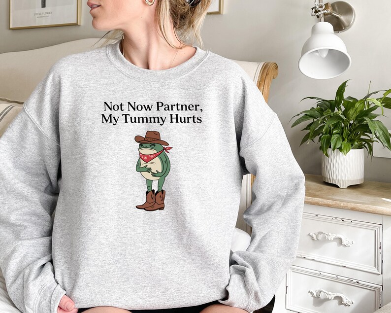 May include: Gray sweatshirt with a frog wearing a cowboy hat and bandana. The text on the sweatshirt reads "Not Now Partner, My Tummy Hurts."