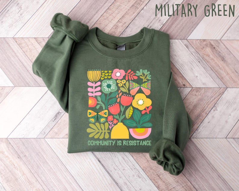 May include: A green sweatshirt with a colorful floral design and the text "Community is Resistance".