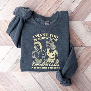 May include: A dark gray sweatshirt with the text "I want you to know that someone cares not me, but someone" and a retro illustration of two women.
