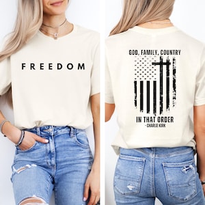 Peut inclure: T-shirt cr&egrave;me avec le mot "FREEDOM" en lettres noires grasses sur le devant. Le dos du t-shirt pr&eacute;sente un motif de drapeau am&eacute;ricain vieilli avec une croix et le texte "GOD, FAMILY, COUNTRY IN THAT ORDER - CHARLIE KIRK."