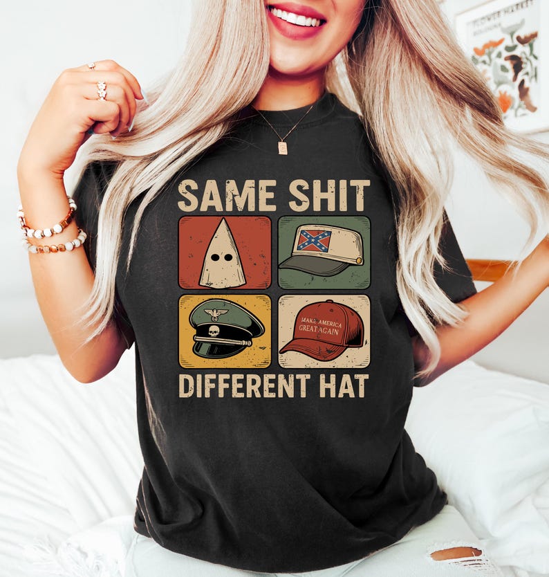 Pu&ograve; includere: T-shirt nera con la scritta "SAME SHIT DIFFERENT HAT" e quattro immagini di cappelli diversi. I cappelli includono un cappuccio bianco, un cappello con la bandiera confederata, un cappello militare e un cappello rosso "Make America Great Again".