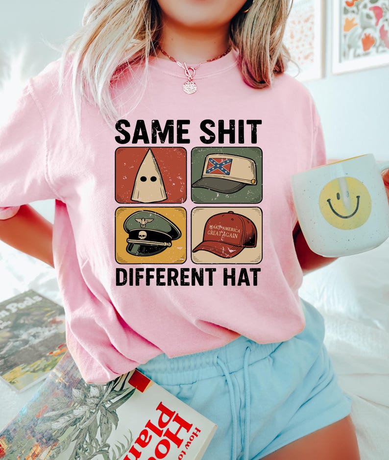 Pu&ograve; includere: Maglietta rosa con la scritta "SAME SHIT DIFFERENT HAT" e quattro immagini di cappelli. Una persona tiene in mano una tazza bianca con una faccina gialla. La persona indossa pantaloncini blu.