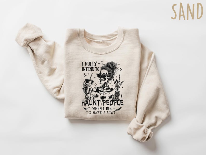 May include: Sand-colored sweatshirt with a black and white graphic of a skeleton wearing sunglasses and holding a drink. The text reads "I FULLY INTEND TO HAUNT PEOPLE WHEN I DIE I HAVE A LIST."