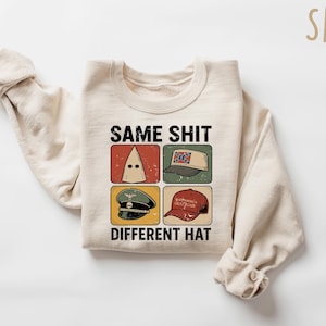 Pu&ograve; includere: Felpa color sabbia con la scritta "SAME SHIT DIFFERENT HAT" e quattro immagini di cappelli diversi. I cappelli includono un cappuccio del KKK, un cappello con la bandiera confederata, un cappello militare e un cappello rosso "Make America Great Again".