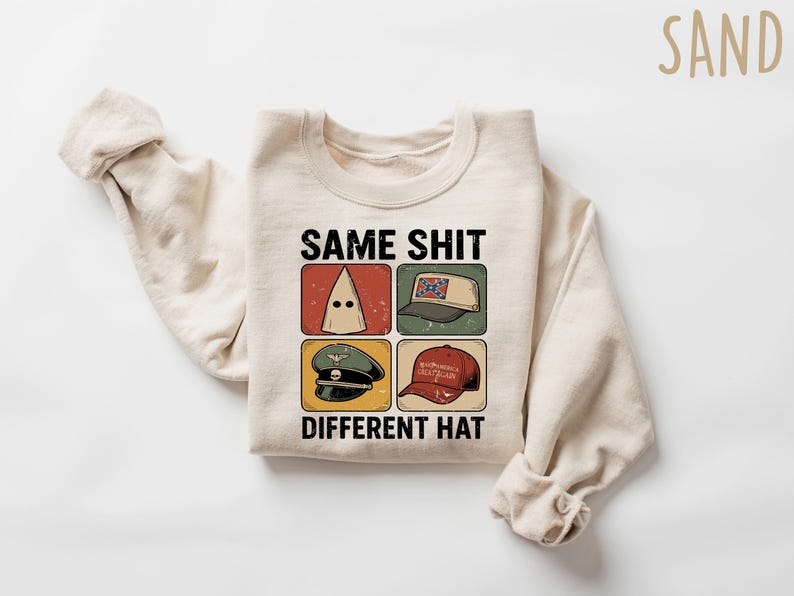 Pu&ograve; includere: Felpa color sabbia con la scritta "SAME SHIT DIFFERENT HAT" e quattro immagini di cappelli diversi. I cappelli includono un cappuccio del KKK, un cappello con la bandiera confederata, un cappello militare e un cappello rosso "Make America Great Again".