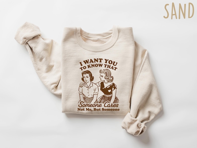 May include: A beige sweatshirt with a brown graphic print of two women. The text on the graphic reads "I want you to know that someone cares. Not me, but someone."
