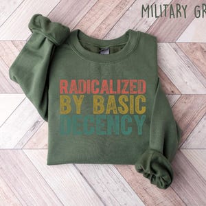 May include: A green sweatshirt with the text "RADICALIZED BY BASIC DECENCY" in a vintage style font with red, orange, yellow, and green colors.