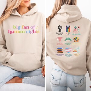 May include: A beige hoodie with a front pocket and a hood. The front of the hoodie has the text "big fan of human rights" in colourful letters. The back of the hoodie has various graphics and text including "Black Lives Matter" and "Love is Love".