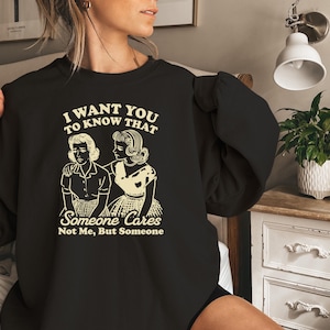 May include: Black sweatshirt with a white graphic print that says "I want you to know that someone cares not me, but someone". The graphic features two women in vintage clothing.