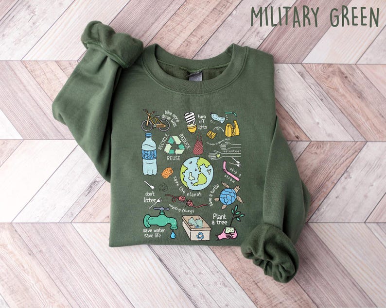Pode incluir: Camisola verde militar com um gr&aacute;fico colorido que promove a conserva&ccedil;&atilde;o ambiental. O design inclui ilustra&ccedil;&otilde;es de uma bicicleta, s&iacute;mbolos de reciclagem, um globo e texto como "Reciclar", "Reduzir" e "Plantar uma &aacute;rvore."