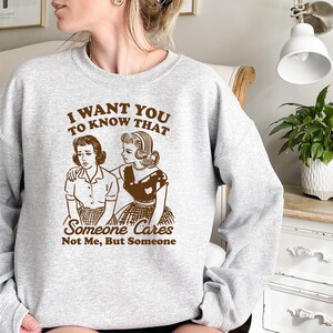 May include: Gray sweatshirt with a brown graphic print of two women. The text on the graphic reads "I want you to know that someone cares not me, but someone."