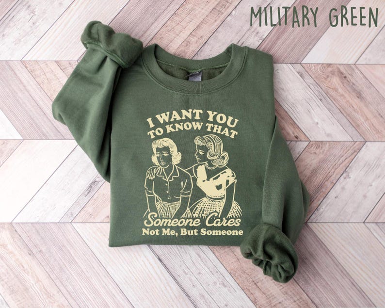 May include: A green sweatshirt with a graphic print of two women. The text on the sweatshirt reads "I want you to know that someone cares, not me, but someone".