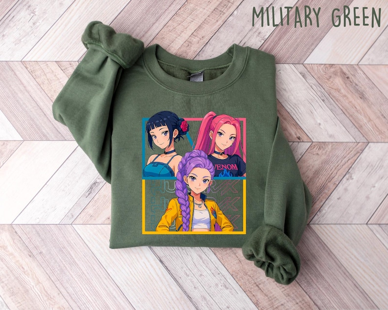 May include: Military green sweatshirt featuring a graphic of three anime-style girls with different hair colors. The graphic is framed in yellow and blue. The sweatshirt is made of a soft material.
