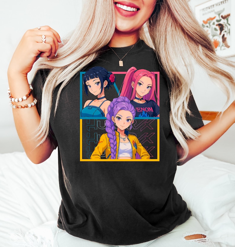 May include: Black t-shirt featuring a colorful graphic of three anime-style women. The graphic is framed in blue and yellow, with the text "JUK" in the background. One woman has dark hair, another has pink hair, and the third has purple hair.