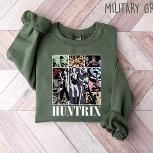 May include: Military green sweatshirt with a graphic featuring a collage of images and the word "HUNTRIX" in white. The sweatshirt is made of a soft material and has a crew neck.