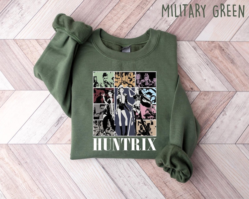 May include: Military green sweatshirt with a graphic featuring a collage of images and the word "HUNTRIX" in white. The sweatshirt is made of a soft material and has a crew neck.
