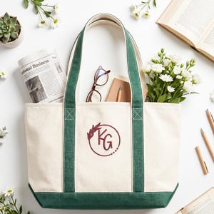 Canvas tote bag with custom monogram logo embroidery, green trim design, styled with books, flowers and stationery, aesthetic branded merchandise