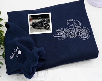 May include: Navy blue sweatshirt with a white embroidered motorcycle design. A small framed photo of a motorcycle is on the sweatshirt. The text "Ride Safe" and a heart are embroidered on the sleeve.