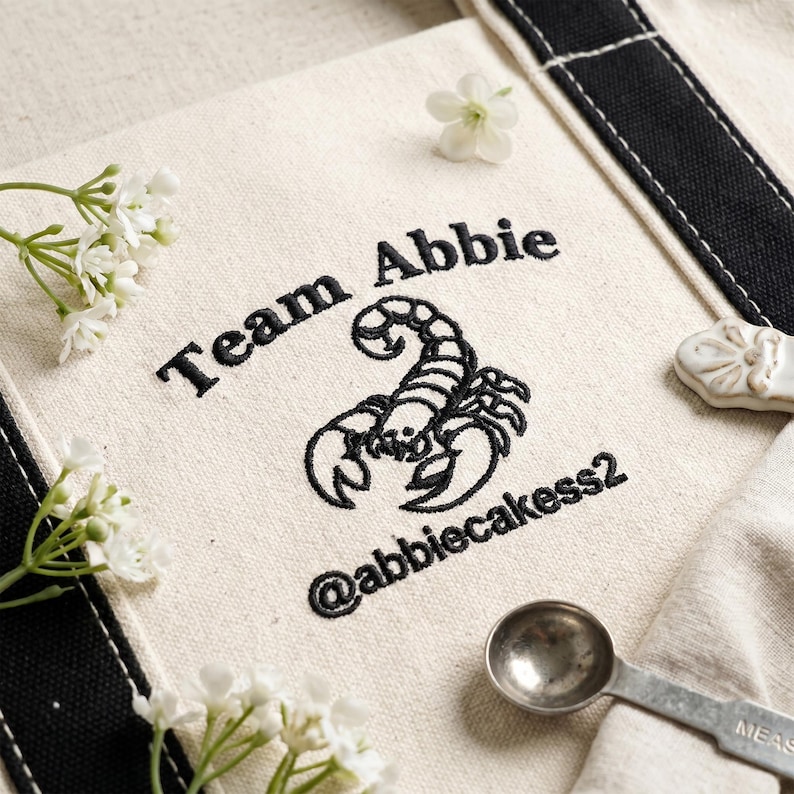 Close-up of embroidered custom logo tote bag with detailed stitching, featuring brand name and social handle, high-quality embroidery texture