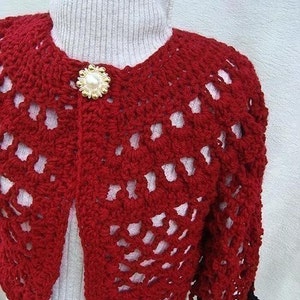 May include: Red crocheted bolero with a white pearl button. The bolero has a lacy design and is cropped.