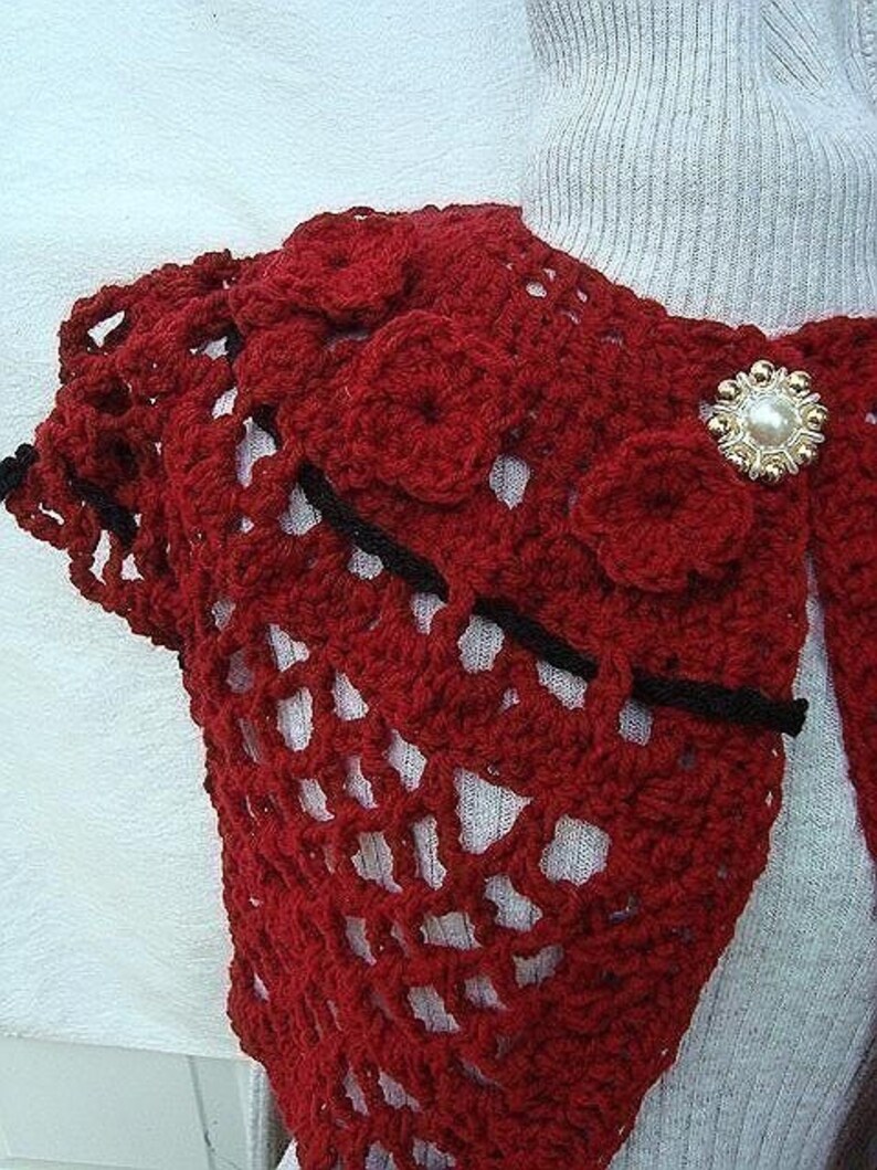 May include: Red crocheted shawl with black trim and a pearl-like button.