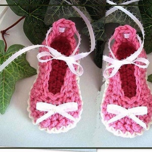 Puede incluir: Un par de zapatos de bebé de ganchillo rosa con ribetes blancos y lazos de cinta de satén blanco.