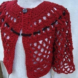 May include: Red crocheted shrug with black trim and a button closure. The shrug is made with a lacy stitch pattern.