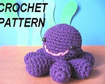May include: Purple crocheted octopus with black eyes and a pink mouth. The octopus is sitting on a brown surface. CROCHET PATTERN is written in black text at the top of the image.