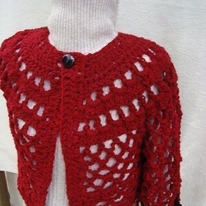 May include: Red crocheted cardigan with a button closure and a lacy pattern. The cardigan is shown on a white mannequin.