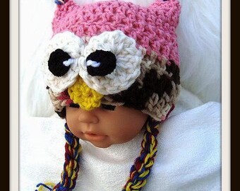 May include: A crocheted owl hat with pink, white, brown, and yellow yarn. The hat has large black eyes and a braided yarn tie. The hat is worn by a baby.