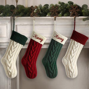 May include: Four personalized Christmas stockings with a cable knit design. The stockings are white, red, and green with the name "Karry" embroidered on each one.