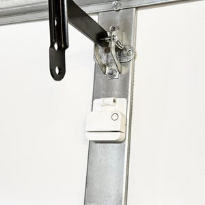 May include: A white smart home device with a round button is mounted on a metal surface. The device is connected to a black metal arm.