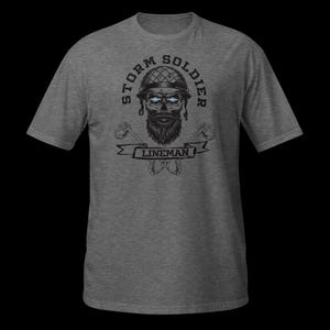 Op de afbeelding: Een grijs gem&ecirc;leerd T-shirt met korte mouwen en een zwarte afbeelding van een schedel met baard en helm met gloeiende blauwe ogen. De tekst STORM SOLDIER staat in een boog boven de schedel en LINEMAN staat op een banner eronder.