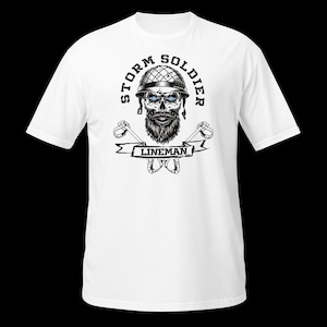 Op de afbeelding: Een wit t-shirt met korte mouwen en een zwart-witte afbeelding van een schedel met een helm en baard. De tekst STORM SOLDIER staat in een boog erboven, met LINEMAN op een banner eronder. Twee gekruiste klimhaken zijn achter de banner geplaatst.