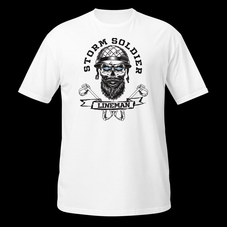 Op de afbeelding: Een wit t-shirt met korte mouwen en een zwart-witte afbeelding van een schedel met een helm en baard. De tekst STORM SOLDIER staat in een boog erboven, met LINEMAN op een banner eronder. Twee gekruiste klimhaken zijn achter de banner geplaatst.