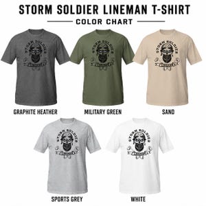 Op de afbeelding: Een kleurenkaart met vijf t-shirts met korte mouwen in grafiet-heather, militair groen, zand, sportgrijs en wit. Elk shirt toont een zwarte afbeelding van een bebaard figuur met een helm en de tekst STORM SOLDIER LINEMAN.