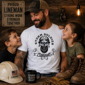 Op de afbeelding: Een wit t-shirt met een opdruk op de borst van een schedel met een helm en baard, voorzien van de tekst "STORM SOLDIER" en "LINEMAN" en twee gekruiste gereedschappen onder de schedel afgebeeld.