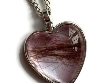 May include: A silver heart-shaped pendant necklace with a clear glass insert containing a lock of brown hair. The pendant is attached to a silver chain.