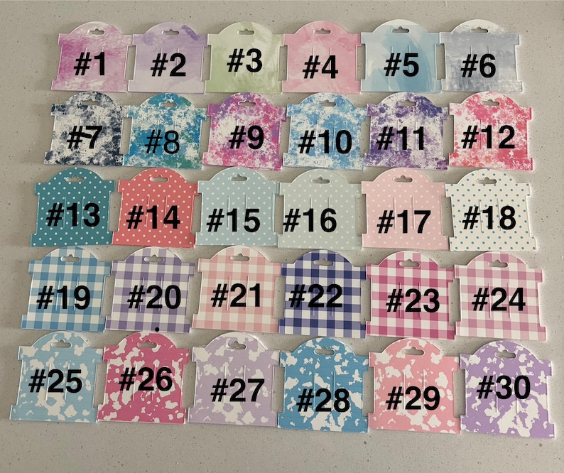 Op de afbeelding: Een verzameling van 30 oorbellen displaykaarten, elk met een uniek ontwerp en nummer van 1 tot 30. De kaarten tonen verschillende patronen, waaronder stippen, ruitjes en aquareleffecten, in een reeks pastelkleuren.