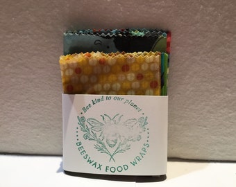 May include: A set of four beeswax food wraps with different colorful patterns. The wraps are folded and stacked on top of each other. The packaging is white with green text that reads "Bee kind to our planet... Beeswax Food Wraps..."