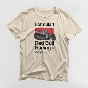 May include: A cream-coloured t-shirt with a Formula 1 Red Bull Racing design. The graphic features a race car image within a red rectangle, with the text "Formula 1" above and "Red Bull Racing" below. A checkered flag design is at the bottom.