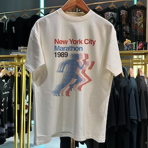 May include: White t-shirt with a red, blue and white graphic print of runners. The graphic includes the text "New York City Marathon 1989".