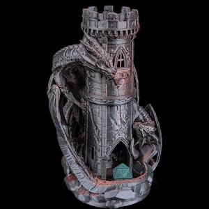 May include: A dark grey dragon-themed dice tower. The tower is cylindrical with a crenellated top and features a dragon wrapped around it. A teal die is visible at the base. The design is gothic and fantasy-inspired.