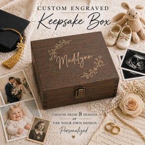 May include: A dark brown wooden keepsake box with the name "Madilynn" engraved on the lid, surrounded by floral accents. The box is rectangular with a metal clasp. The image includes photos, a graduation cap, and a stuffed animal.