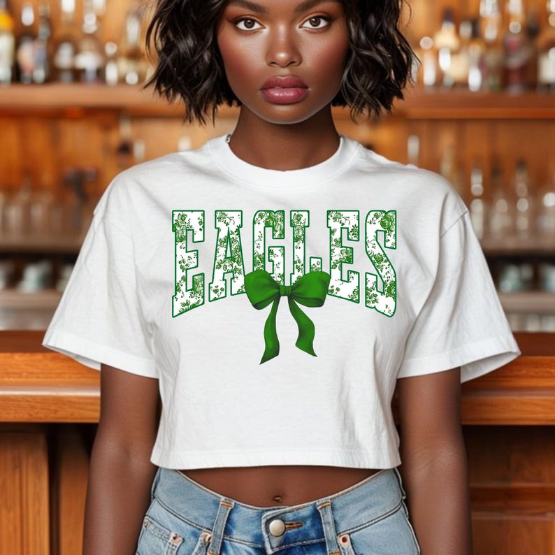 May include: White cropped t-shirt with a green and white "EAGLES" graphic with a green bow.